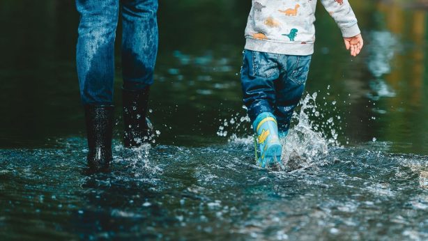 An image of a mother and daughter splashing through a flood with wellies on